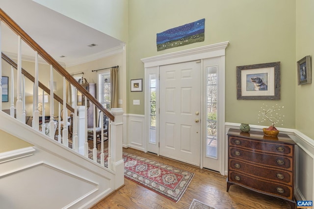 foyer featuring stairway, wood finished floors, a wainscoted wall, visible vents, and crown molding