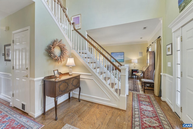 entrance foyer featuring wainscoting, stairway, ornamental molding, and wood finished floors