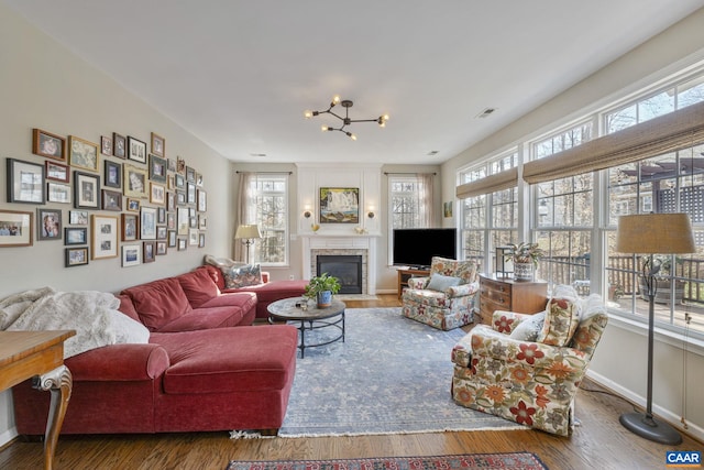 living room featuring wood finished floors, visible vents, baseboards, a fireplace with flush hearth, and a chandelier