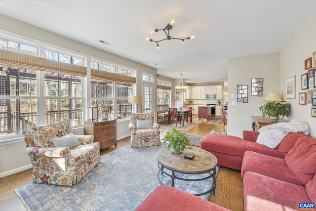 living area with light wood-type flooring, visible vents, baseboards, and a notable chandelier