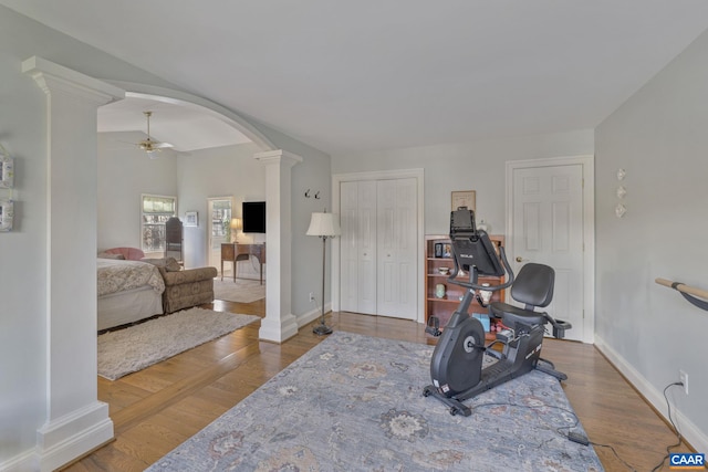 exercise room with wood finished floors, a ceiling fan, arched walkways, and ornate columns