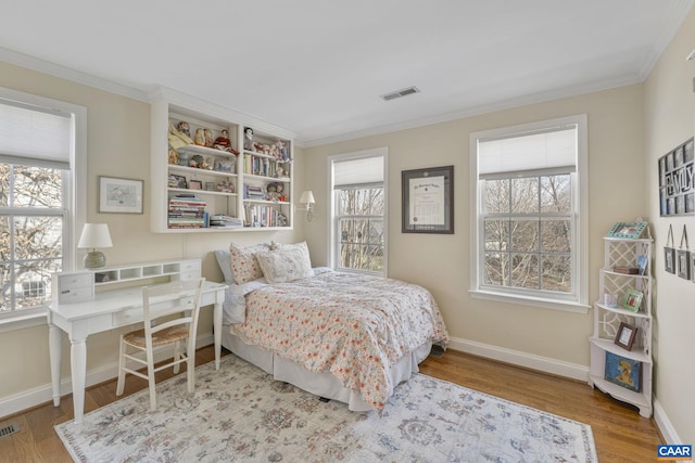 bedroom with visible vents, baseboards, wood finished floors, and crown molding