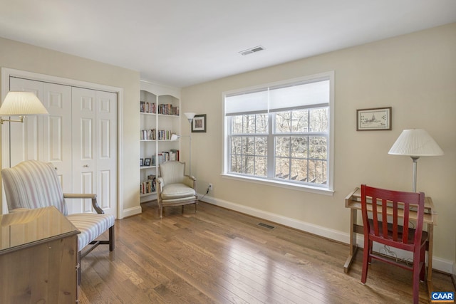 sitting room with hardwood / wood-style flooring, built in shelves, visible vents, and baseboards