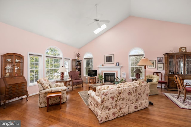 living room with a glass covered fireplace, plenty of natural light, wood finished floors, and high vaulted ceiling