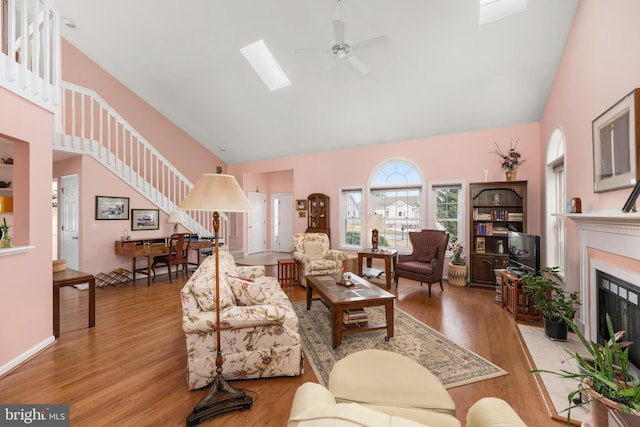 living room with a fireplace with flush hearth, ceiling fan, high vaulted ceiling, and light wood-style floors