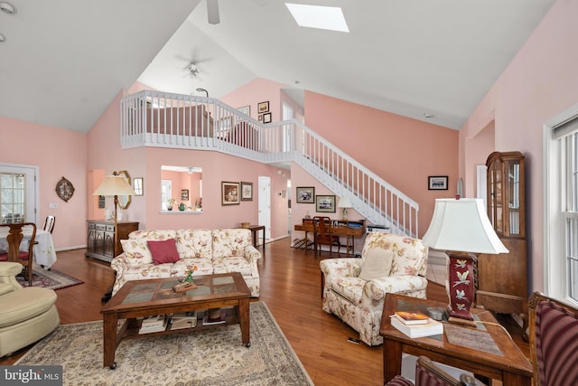 living room with stairway, a skylight, wood finished floors, high vaulted ceiling, and a ceiling fan