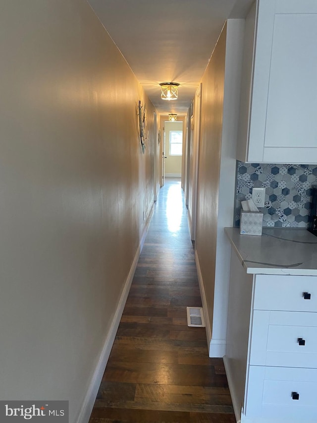 hallway with dark wood finished floors, baseboards, and visible vents