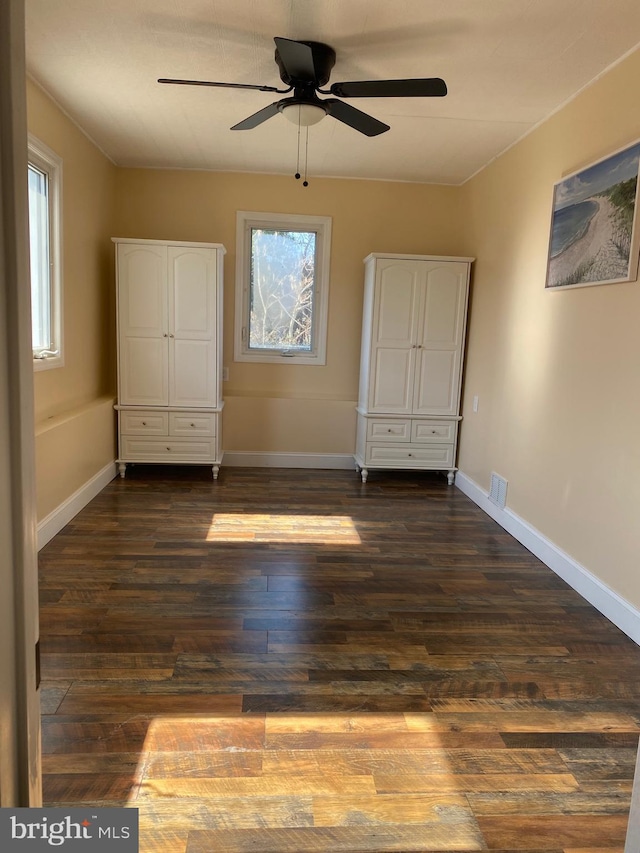 unfurnished bedroom with visible vents, baseboards, dark wood-type flooring, and ceiling fan