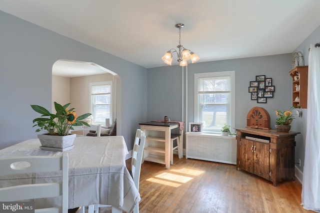 dining room featuring an inviting chandelier, light wood-style flooring, radiator heating unit, and arched walkways