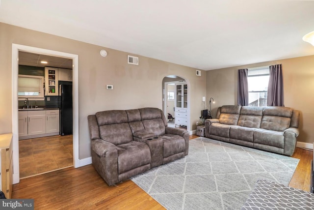 living room featuring wood finished floors, visible vents, arched walkways, and baseboards