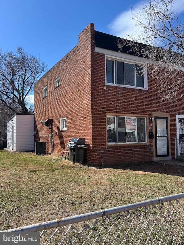 view of home's exterior featuring brick siding, central AC unit, a lawn, and fence