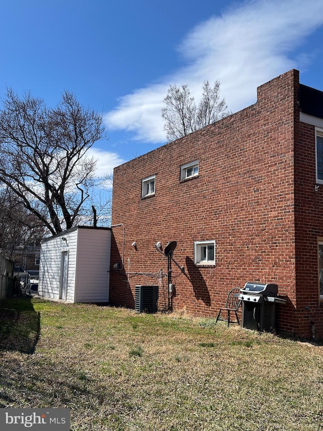 back of property featuring central air condition unit, a yard, and brick siding