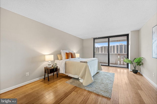 bedroom featuring a view of city, access to outside, a textured ceiling, light wood-style floors, and baseboards