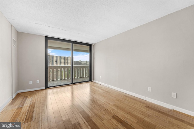 spare room featuring visible vents, baseboards, hardwood / wood-style floors, expansive windows, and a textured ceiling