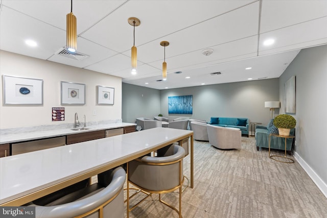 kitchen featuring visible vents, pendant lighting, a sink, baseboards, and light colored carpet