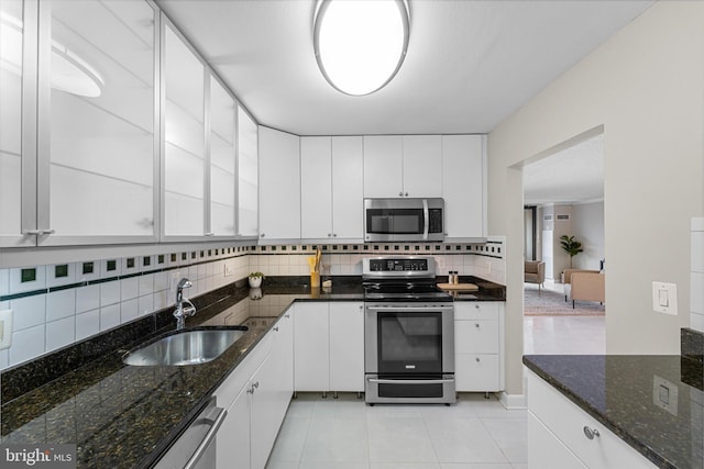 kitchen featuring light tile patterned floors, a sink, decorative backsplash, white cabinets, and appliances with stainless steel finishes