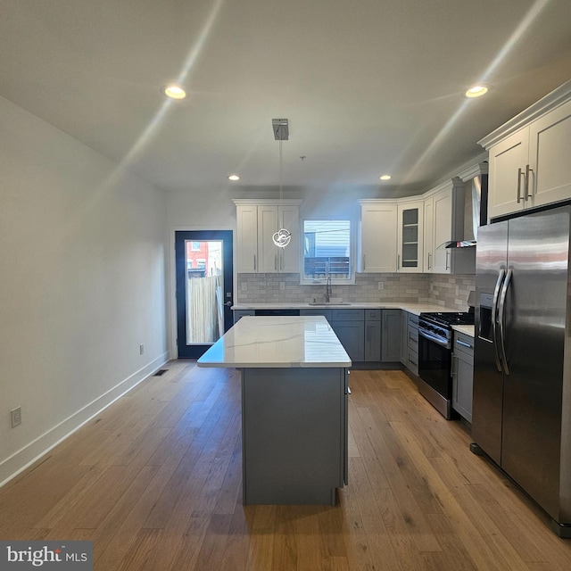 kitchen featuring a kitchen island, a sink, appliances with stainless steel finishes, wall chimney range hood, and tasteful backsplash