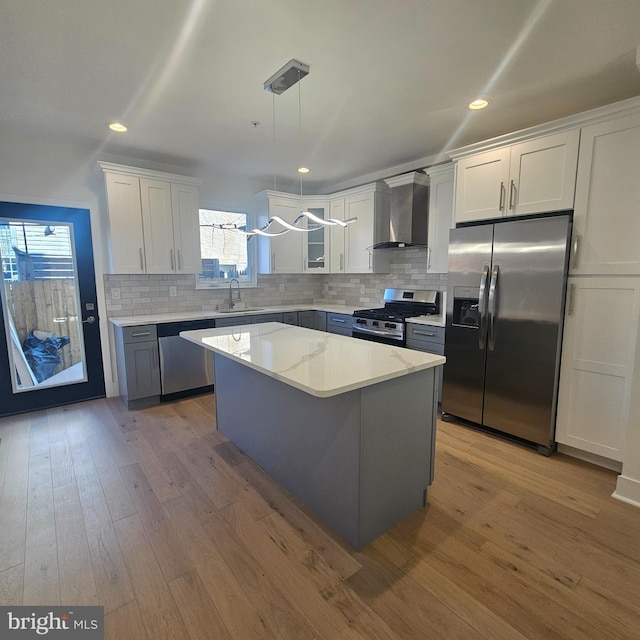 kitchen with wood finished floors, stainless steel appliances, wall chimney range hood, and a sink