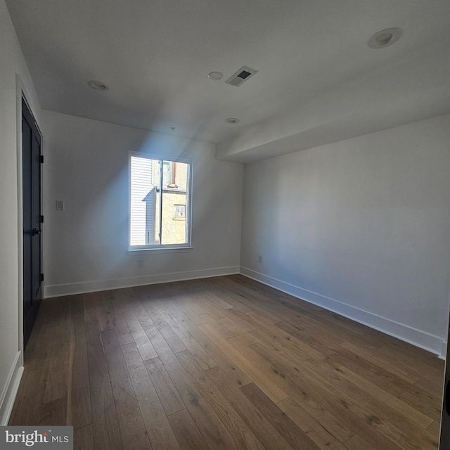 empty room with dark wood finished floors, visible vents, and baseboards