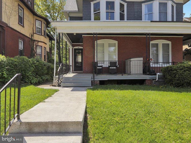 view of exterior entry with a porch, a lawn, and brick siding