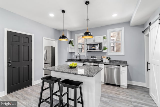 kitchen with baseboards, a breakfast bar, appliances with stainless steel finishes, a barn door, and a center island