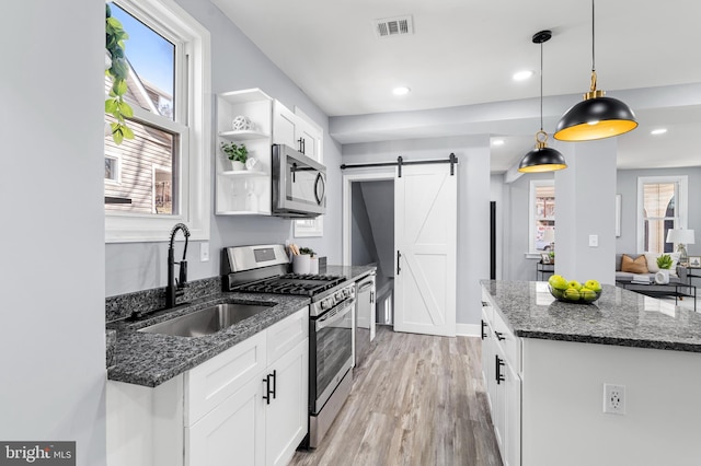 kitchen featuring visible vents, a barn door, stainless steel appliances, white cabinetry, and a sink