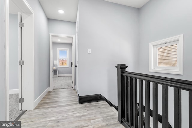 corridor with an upstairs landing, baseboards, and light wood finished floors