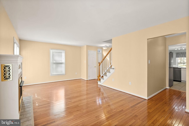 unfurnished living room with light wood-style flooring, baseboards, a fireplace, and stairs