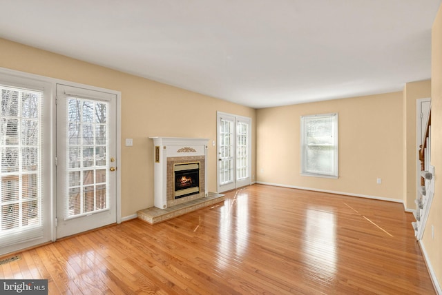 unfurnished living room with a tiled fireplace, visible vents, baseboards, and hardwood / wood-style flooring