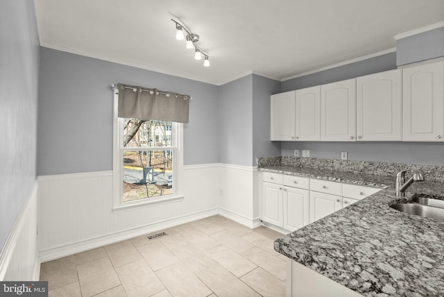 kitchen featuring a wainscoted wall, stone countertops, white cabinetry, and a sink