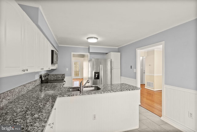 kitchen featuring visible vents, a peninsula, a sink, appliances with stainless steel finishes, and wainscoting