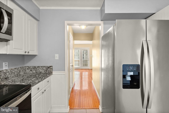 kitchen with appliances with stainless steel finishes, ornamental molding, wainscoting, and white cabinetry