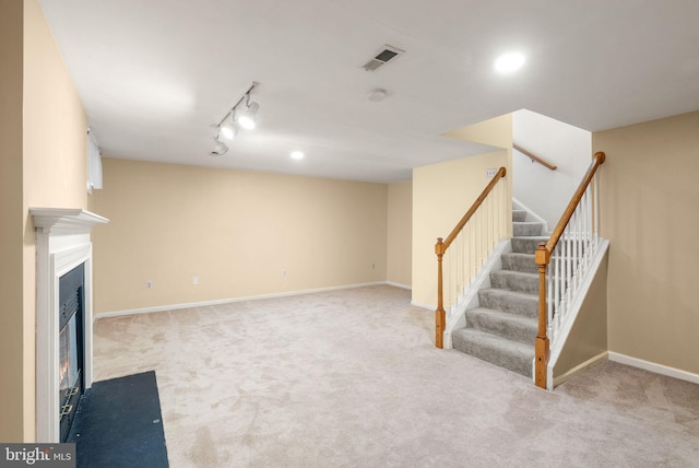 finished below grade area featuring visible vents, a fireplace with flush hearth, carpet floors, and stairway