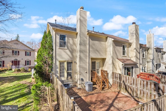 back of property with central AC unit, a chimney, a yard, and fence