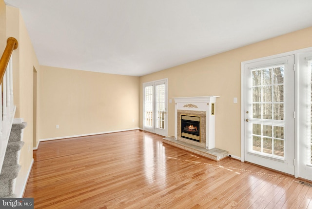 unfurnished living room with stairway, visible vents, baseboards, light wood-style flooring, and a glass covered fireplace