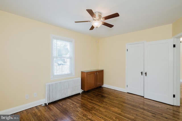 unfurnished bedroom with ceiling fan, radiator, dark wood-type flooring, and baseboards