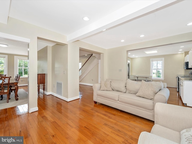 living room with visible vents, baseboards, beamed ceiling, stairs, and light wood-style flooring