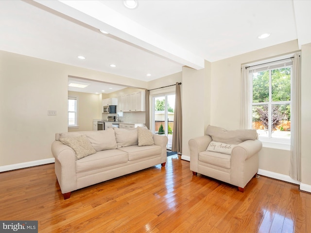 living room with beam ceiling, light wood-type flooring, and baseboards