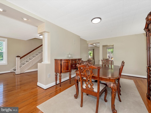 dining room with stairway, wood finished floors, baseboards, and ornate columns