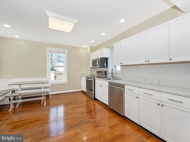 kitchen with light wood finished floors, recessed lighting, a sink, stainless steel appliances, and white cabinets