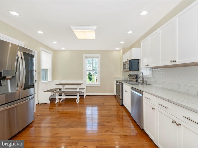 kitchen with light wood finished floors, decorative backsplash, appliances with stainless steel finishes, white cabinetry, and a sink