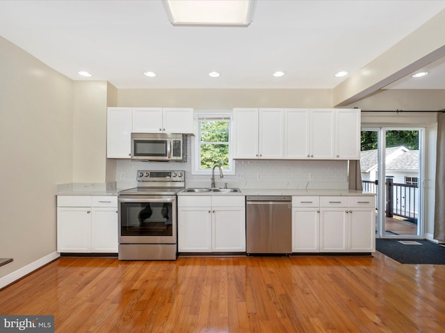 kitchen with light wood finished floors, tasteful backsplash, light countertops, appliances with stainless steel finishes, and a sink