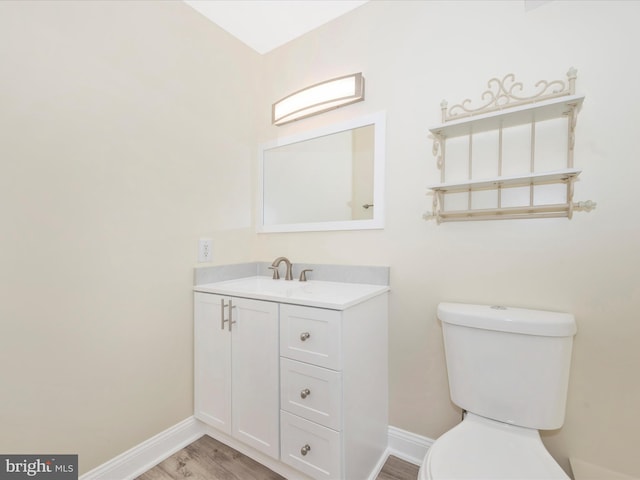 half bath with vanity, toilet, wood finished floors, and baseboards