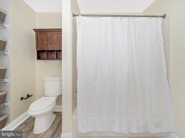 bathroom with baseboards, toilet, wood finished floors, and shower / bath combination with curtain