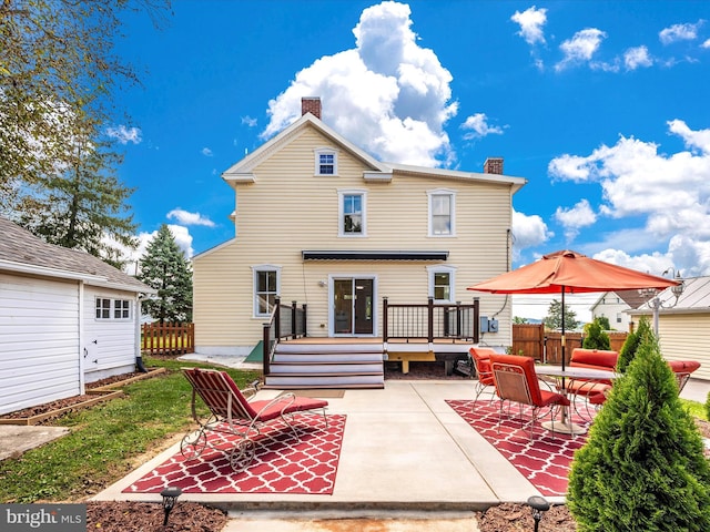 back of house with a deck, a patio, fence, and a chimney