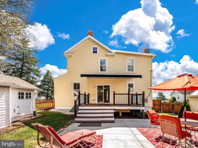 rear view of property featuring a patio, a deck, a chimney, and fence