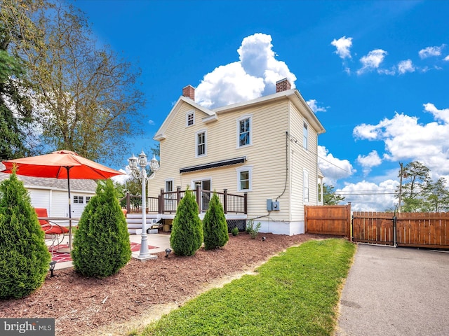 rear view of house with fence, a chimney, a deck, a patio, and a gate