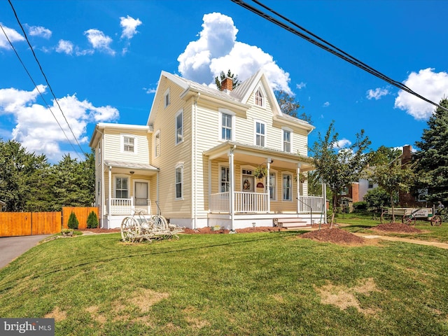 view of front of house with a porch, fence, a front lawn, and a chimney