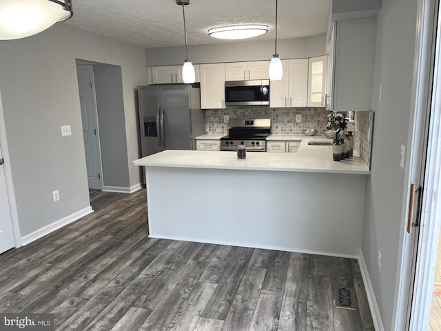 kitchen featuring backsplash, dark wood finished floors, light countertops, appliances with stainless steel finishes, and a peninsula