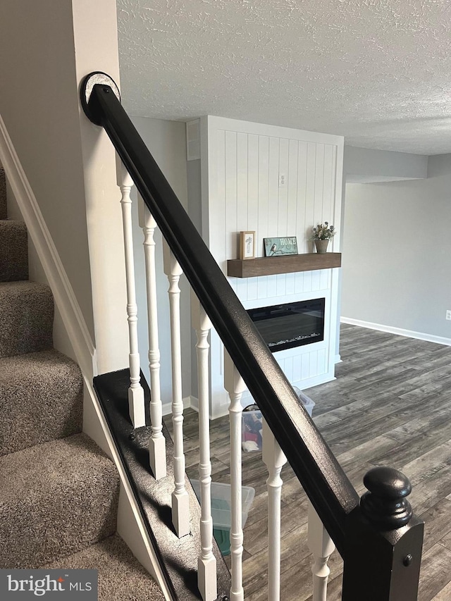 stairway with a glass covered fireplace, a textured ceiling, baseboards, and wood finished floors